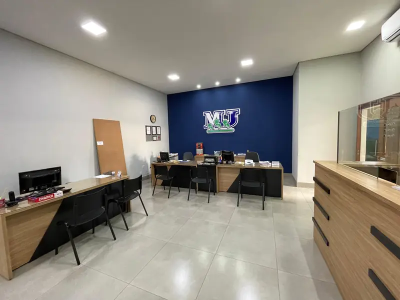 Balcão e mesas de atendimento da loja, com computadores, parede azul com o monograma MU e bancada de madeira ao lado.